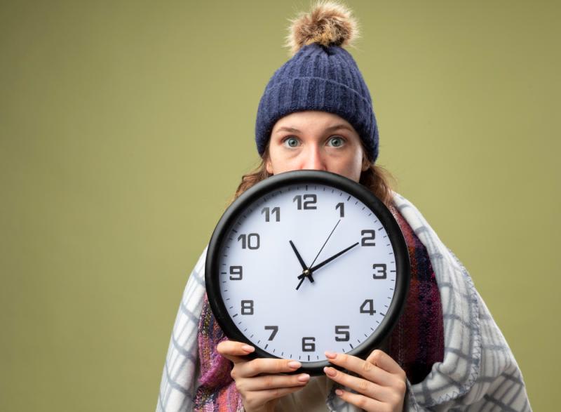 Joven con gorro y manta sosteniendo un reloj